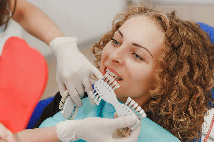 The Dentist Comparing Patient S Teeth Shade With Samples For Bleaching Treatment